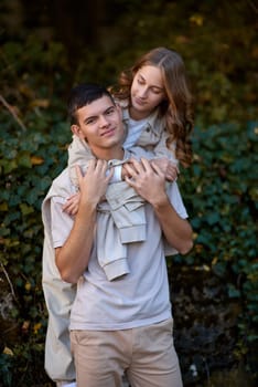 Young Cute Female Hugs Boyfriend. In Autumn Outdoor. Lovers Walking in Park. Attractive Funny Couple. Lovestory in Forest. Man and Woman. Cute Lovers in the Park. Family Concept. Happy Couple.