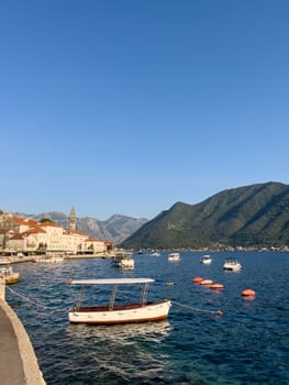 Small boats are moored off the coast of Perast against the backdrop of old houses and the church of St. Nicholas. Montenegro. High quality photo
