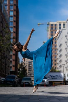 Beautiful Asian ballerina in blue dress posing in splits outdoors. Urban landscape. Vertical photo