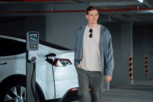 Young man travel with EV electric car to shopping center parking lot charging in downtown city showing urban sustainability lifestyle by green clean rechargeable energy of electric vehicle innards