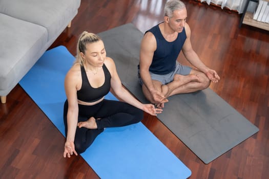 Happy active senior couple in sportswear being doing yoga in meditation posture on exercising mat at home. Healthy senior pensioner lifestyle with peaceful mind and serenity. Clout