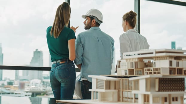 Group of caucasian diverse architect engineer pointing at skyscraper at day time. Skilled manager team looking at city or skyscraper while house model was placed on table. Back view. Tracery