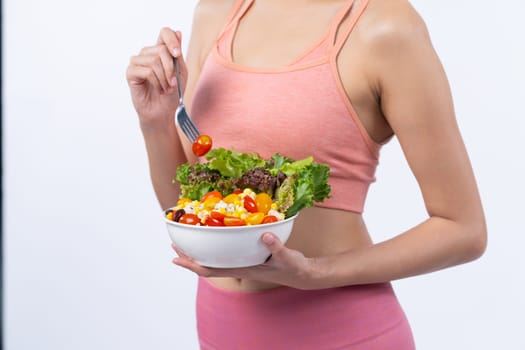 Young sporty Asian woman in sportswear holding salad bowl fill with vibrant of fruit and vegetable. Natural youthful and fit body lifestyle with balance nutrition on isolated background. Vigorous