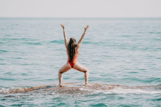 Woman sea yoga. Back view of free calm happy satisfied woman with long hair standing on top rock with yoga position against of sky by the sea. Healthy lifestyle outdoors in nature, fitness concept.