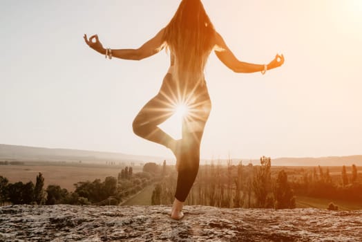 Well looking middle aged woman with long hair, fitness instructor in leggings and tops doing stretching and pilates on the rock near forest. Female fitness yoga routine concept. Healthy lifestyle.