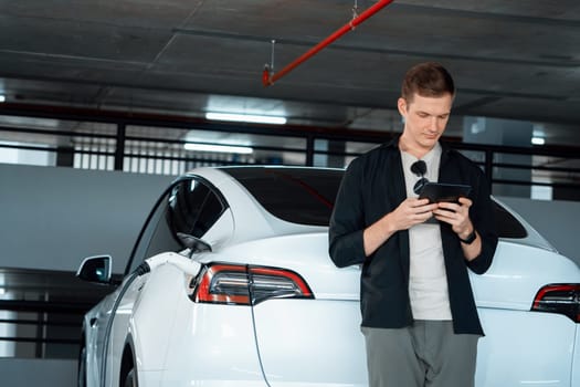 Young man travel with EV electric car to shopping center parking lot charging in downtown city showing urban sustainability lifestyle by green clean rechargeable energy of electric vehicle innards