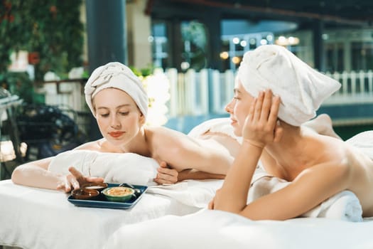 Couple of beautiful young girls lie on spa bed during interested in homemade beauty facial mask. Attractive woman touching herbal facial mask. Surrounded with nature environment. Tranquility.