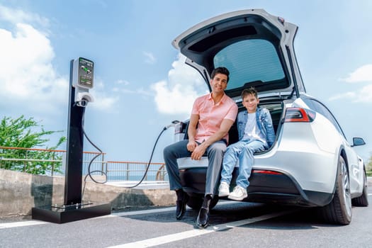 Family road trip vacation traveling by the sea with electric car, father and son recharge EV car with green and clean energy. Natural travel and eco-friendly car for sustainable environment. Perpetual