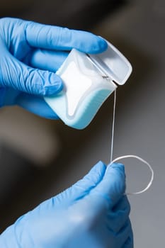 Dental floss in the hands of a dentist clad in latex gloves. Teeth care concept