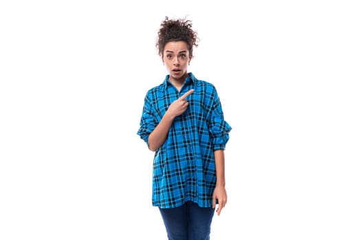 a young woman with curly black hair dressed in a blue shirt points her hand to the side. advertising concept.