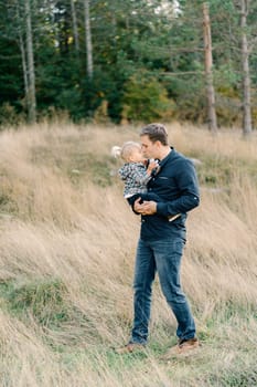 Dad kisses a little girl on the nose holding her in his arms while walking on the lawn. High quality photo
