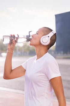 young sports woman drinking water from her bottle and listening to music on her headphones, concept of active and healthy lifestyle, copy space for text