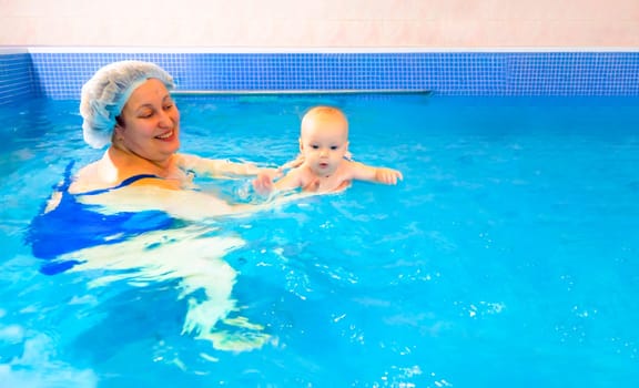 Adorable baby girl enjoying swimming in a pool with her mother early development class for infants teaching children to swim and dive. Swimming instructor doing exercises with a small child in the pool . High quality photo