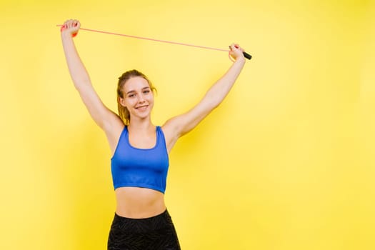 Portrait of gentle muscular woman holding skipping rope on her neck over yellow background