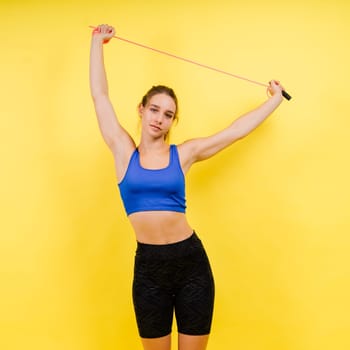 Portrait of gentle muscular woman holding skipping rope on her neck over yellow background