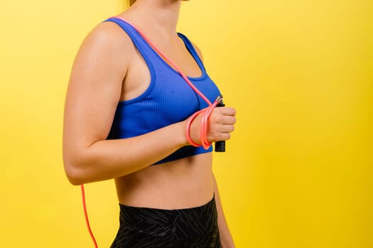 Portrait of gentle muscular woman holding skipping rope on her neck over yellow background