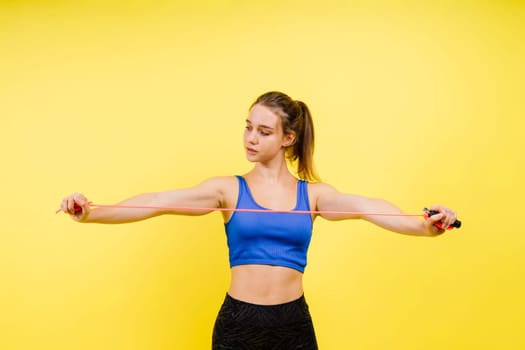 Portrait of gentle muscular woman holding skipping rope on her neck over yellow background