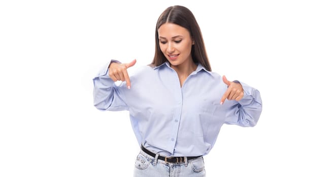 pretty young brunette european woman dressed in a blue shirt shows with her hands to the place for advertising on an isolated background with copy space.