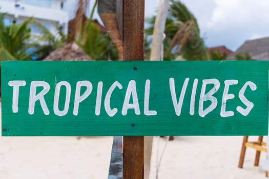 Green sign with white writing "tropical vibes" on sandy beach at sunny day,relax and summer concept.