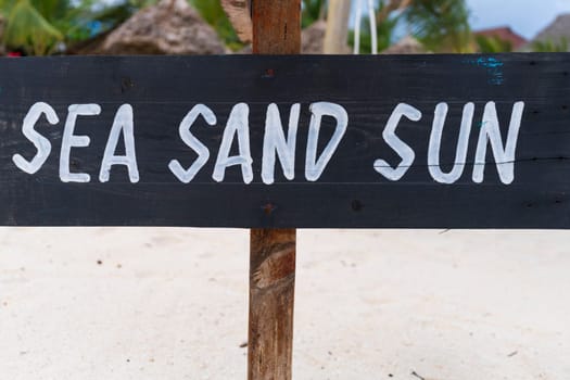 Black sign with white writing "sea sand sun" on sandy beach at sunny day,relax and summer concept.