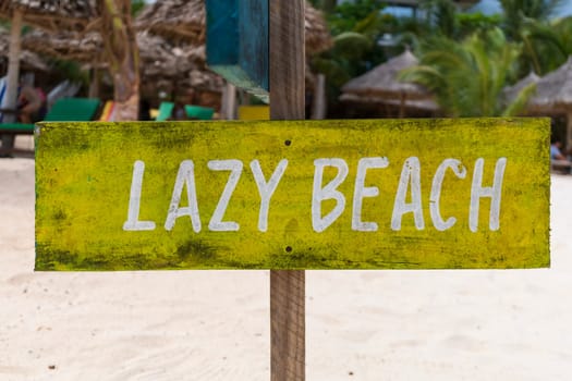 yellow sign with white writing "lazy beach" on sandy beach at sunny day,relax and summer concept.