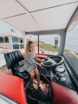 Little girl sits behind the wheel of a tractor in the cab. High quality photo