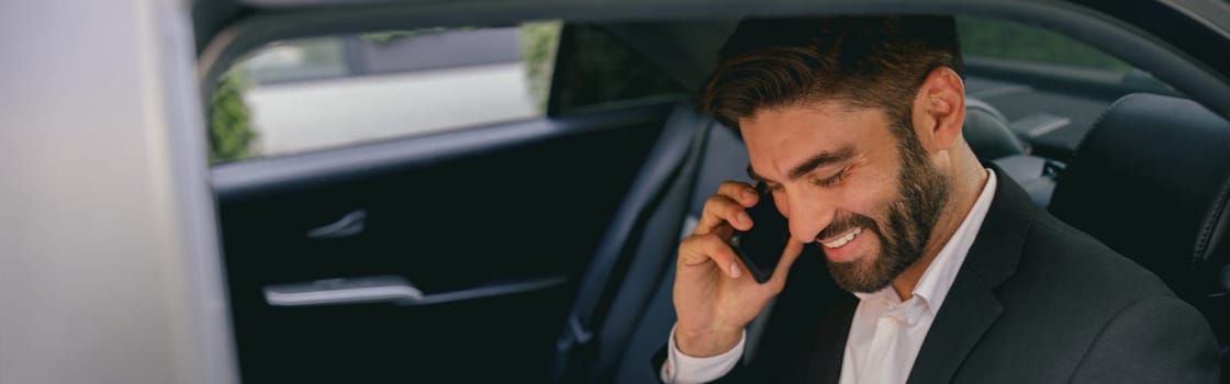 Handsome businessman in suit using personal computer and making phone call in taxi