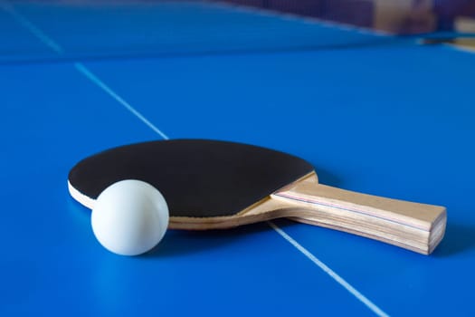 Wooden racket for ping pong and white ball lying on the blue table.