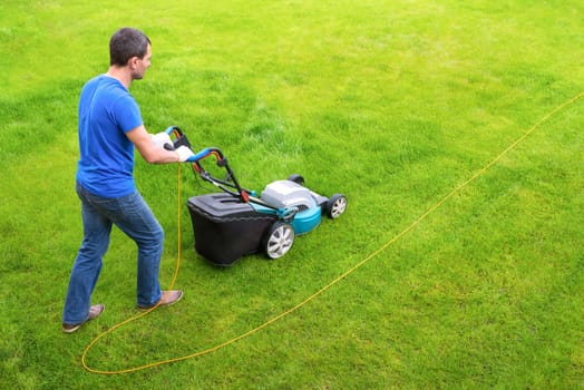 Gardener in the garden mows grass with a lawn mower. Side view.