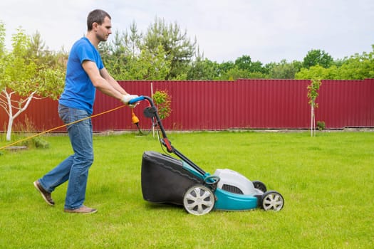 Worker with a lawn mower mows grass in the garden.