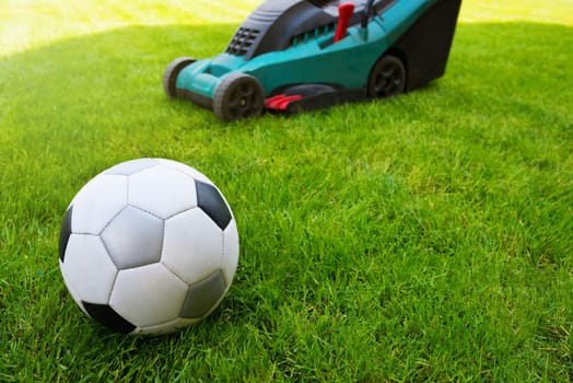 Soccer ball and lawn mower on a field in the grass. Close-up. Grass care.