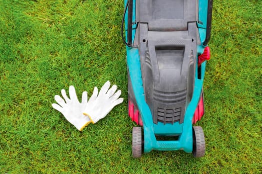 Working white gloves and lawn mower on the grass. Top view.