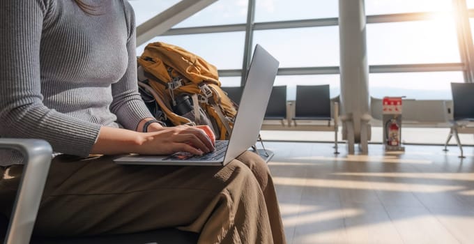 Young Asian woman using laptop to check flight times in airport for vacation.