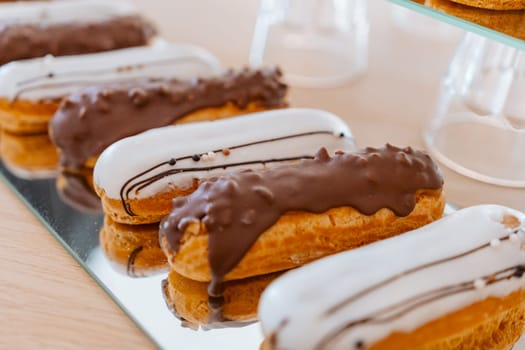 Eclairs with white and chocolate icing are laid out in a row on a mirror surface, display in a store