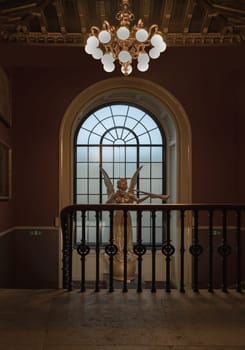 London, UK - Nov 27, 2023 - View of Angel statue in front of wooden window on red wall at the Victoria and Albert Museum. Abstract interior design, Space for text, Selective focus.