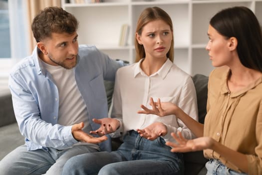 Misunderstanding In Friendship. Three Angry Friends Having Quarrel Arguing Sitting On Sofa At Home. Millennial Romantic Couple and Female Friend Engage in Heated Argument Having Conflict