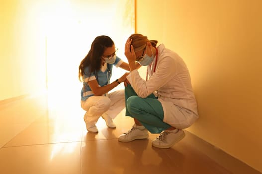 Doctor squat in hallway of hospital and cry. Nurse soothe woman.