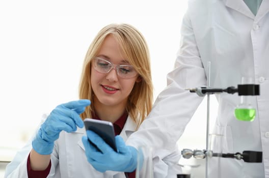A female doctor in a chemical laboratory holds a smartphone in his hand with display, you can insert a picture or an image you want to write for an advertising company