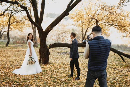 Professional wedding photographer taking pictures of the bride and groom in nature in autumn