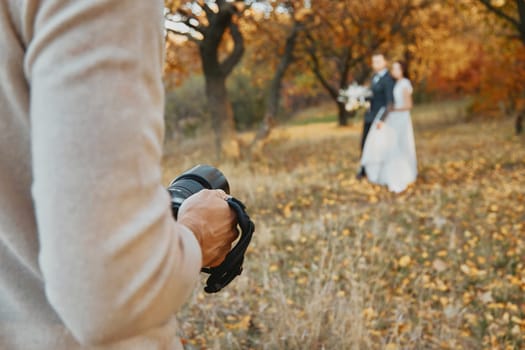 Professional wedding photographer taking pictures of the bride and groom in nature in autumn