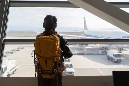 Traveler woman plan and backpack see airplane flight at the airport glass window.