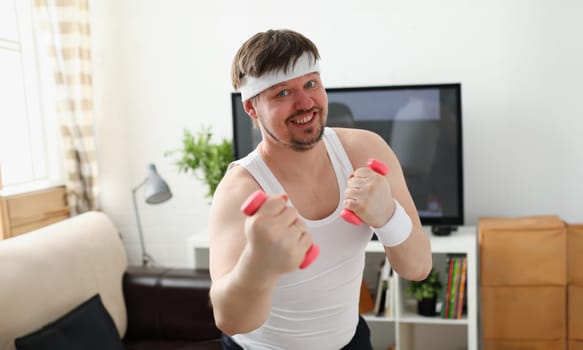 Young attractive man engaged in fitness at home holding dumbbell in hand trying to fight excess weight and loss