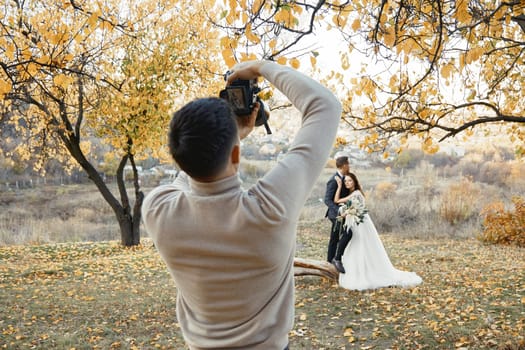 Professional male wedding photographer taking pictures of the bride and groom in nature