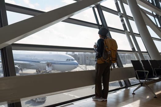 Traveler woman plan and backpack see airplane flight at the airport glass window.