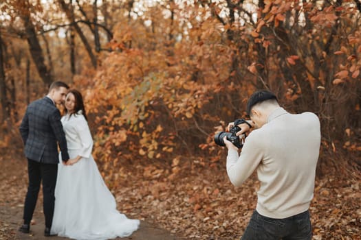 Professional wedding photographer taking pictures of the bride and groom in nature in autumn