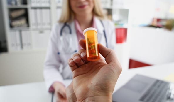 male medicine doctor hand hold jar of pills and write prescription to patient at worktable. Panacea and life save, prescribing treatment, legal drug store concept. Empty form ready to be used