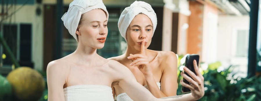 Couple of young beautiful women with beautiful skin in white towel taking a photo together at outdoor surrounded by peaceful natural environment. Beauty and healthy spa concept. Tranquility.