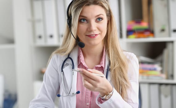 A beautiful feminine blonde doctor talking to patient over wireless headset advises a medical problem the formation of remote education internship callcenter specialist