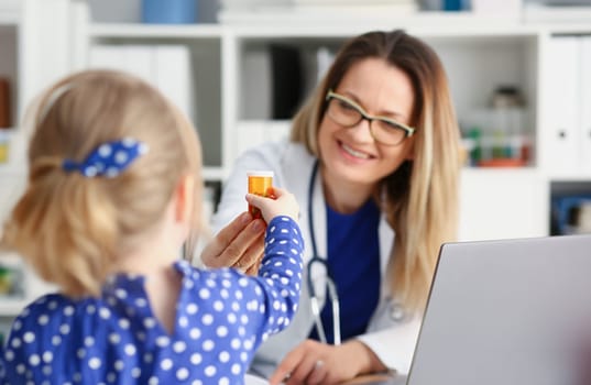 Beautiful smiling female doctor hold in arms pill bottle and offer it to child visitor closeup. Panacea or life save antidepressant from legal store prescribe vitamin medic aid for healthy lifestyle