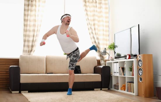 Young handsome man in shorts and vest holds pink dumbbells in hand. Watch tv lessons single combats is practicing receptions of sensei one home fitness indoor training independent education remotely